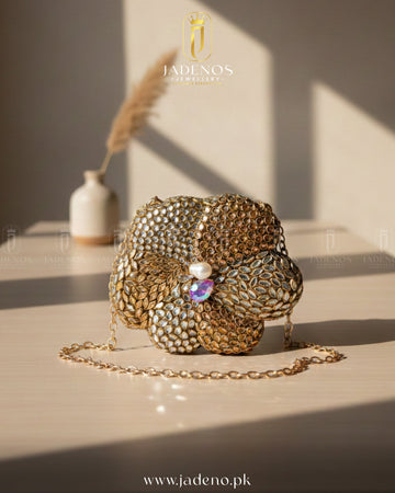The Scarlet Core Clutch with gold floral design, crystal embellishments, pearl center, and delicate chain strap in soft lighting.